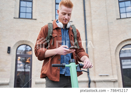 Man holding cell phone and unlocks with it powered scooter 78645217