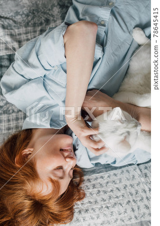 Woman laying at the bed and scratching her white fluffy cat 78645415