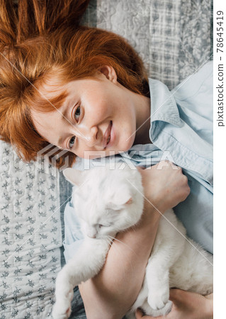 Woman laying at the bed and embracing her white fluffy cat 78645419