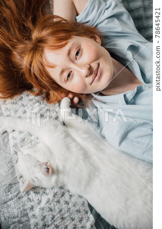 Woman looking at the camera and laying at the back at the bed near her white cat Woman looking at the camera and laying at the back at the bed near her white cat 78645421