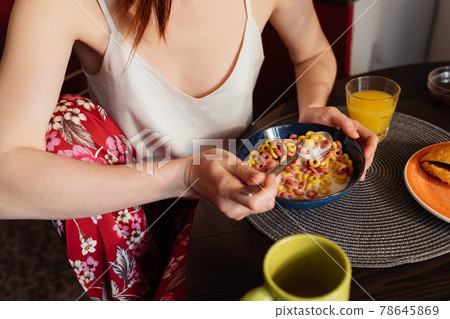 Caucasian woman with ginger hair eating corn flakes cereal while sitting at the table 78645869