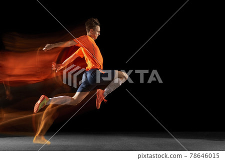Young caucasian male football or soccer player kicking ball for the goal in mixed light on dark background. Concept of healthy lifestyle, professional sport, hobby. 78646015