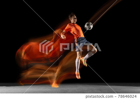 Young caucasian male football or soccer player kicking ball for the goal in mixed light on dark background. Concept of healthy lifestyle, professional sport, hobby. 78646024