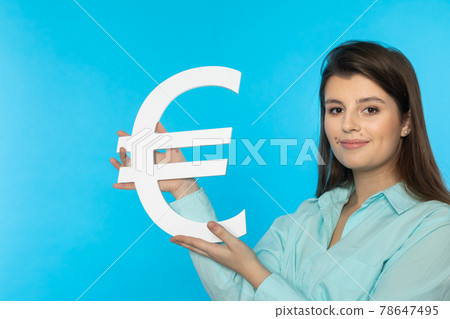 The girl holds a large euro symbol in her hands. Shape of the currency of the European Union. Symbol of finance and cash flow in the economy and the stock market on a solid background. The girl holds a large euro symbol in her hands. Shape of the currency of the European Union. Symbol of finance and cash flow in the economy and the stock market on a solid background. 78647495