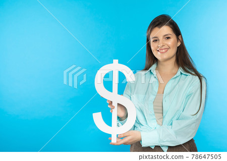 The girl holds a large dollar symbol in her hands. The shape of the US currency. Symbol of finance and cash flow in the economy and the stock market on a blue background. 78647505