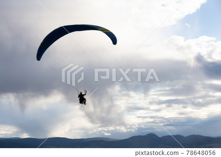 Adventurous Man Flying on a Paraglider around the mountains. 78648056