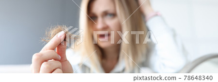 Frustrated woman holds bun of her hair in her hand 78648340