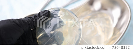 Gloved doctor holds silicone breast implant closeup 78648352