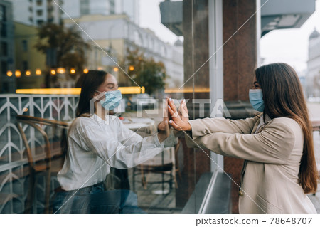 Two women in protective masks opposite each other, window between them. Two women in protective masks opposite each other, window between them. 78648707