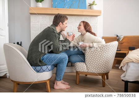 Smiling man and touching woman drinking coffee near fireplace 78650038