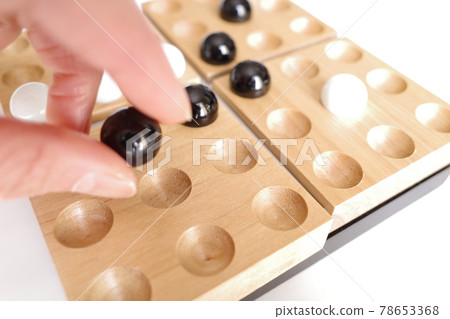 A board game where white and black marbles are lined up on a wooden tray 78653368