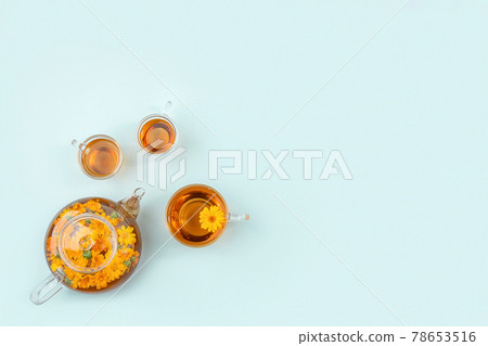 Cups of herbal tea, transparent teapot with calendula flowers on blue background. Calming drink concept. Copy space Flat lay Top view Cups of herbal tea, transparent teapot with calendula flowers on blue background. Calming drink concept. Copy space Flat lay Top view 78653516