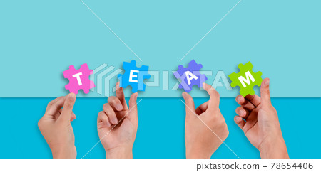 Close up of five hands holding jigsaw puzzle with text TEAM on blue background. 78654406