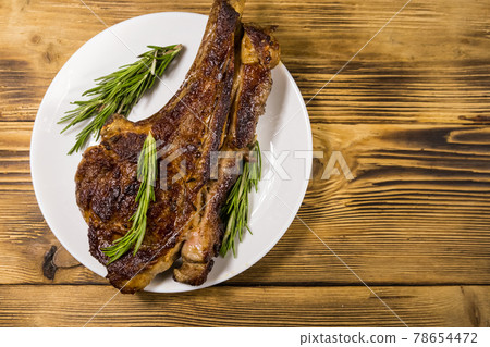 Roasted beef rib eye steak on bone with rosemary in white plate on wooden table Roasted beef rib eye steak on bone with rosemary in white plate on wooden table 78654472