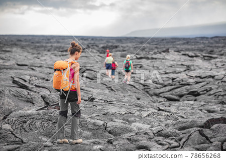 Hiking group of hikers walking on Hawaii volcano lava field hike adventure happy woman with backpack in Big Island, Hawaii. Tourists walking on guided tour trail outdoor USA summer travel vacation 78656268