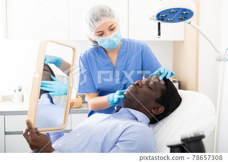 Woman beautician in mask examining face skin of afro american male patient Woman beautician in mask examining face skin of afro american male patient 78657308