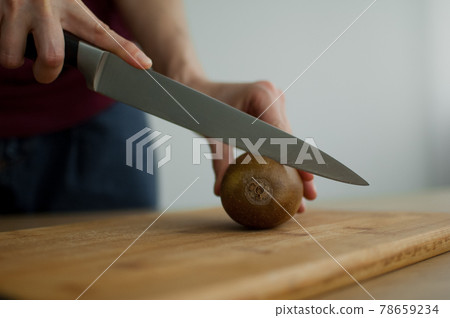 Female hands is cutting a fresh ripe golden kiwi fruit on a cut wooden board. Exotic fruits, healthy eating concept Female hands is cutting a fresh ripe golden kiwi fruit on a cut wooden board. Exotic fruits, healthy eating concept 78659234