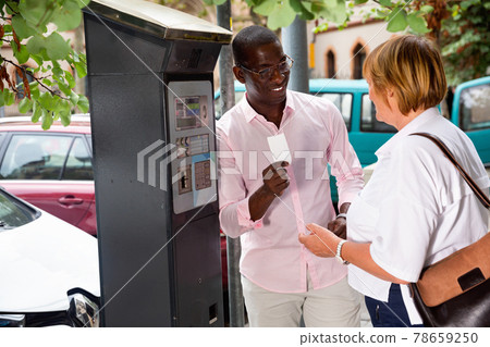 Polite intelligent African man helping middle aged woman to buy ticket in parking meter on summer city street Polite intelligent African man helping middle aged woman to buy ticket in parking meter on summer city street 78659250