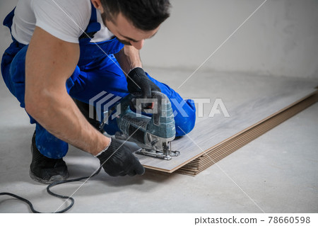 Handyman in blue uniform cuts laminate with jigsaw Handyman in blue uniform cuts laminate with jigsaw 78660598