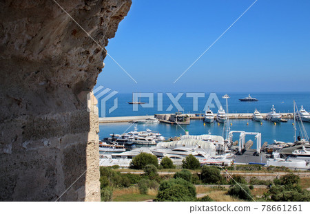View on a port and yacht parking on blue sky and sea water background through big aged brick wall arched tower window 78661261