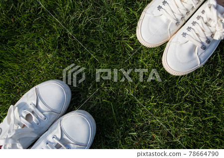 Women's and men's white sneakers on green grass. The guy and the girl are facing each other. View from above. 78664790