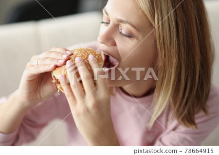 Young woman eating delicious appetizing hamburger at home 78664915