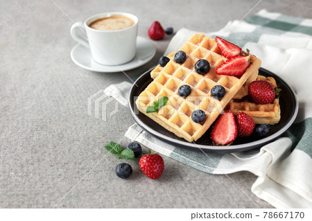 Waffles plate, strawberry, blueberry, mint leaf, coffee cup on gray background Waffles plate, strawberry, blueberry, mint leaf, coffee cup on gray background 78667170