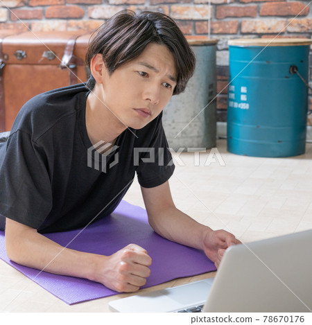 A young man who lays down in his living room early in the morning and checks the muscle training video on his computer to think about it. A young man who lays down in his living room early in the morning and checks the muscle training video on his computer to think about it. 78670176