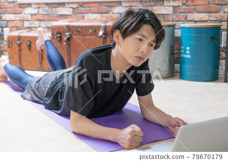 A young man checking muscle training videos on his computer while lying down in his living room early in the morning A young man checking muscle training videos on his computer while lying down in his living room early in the morning 78670179