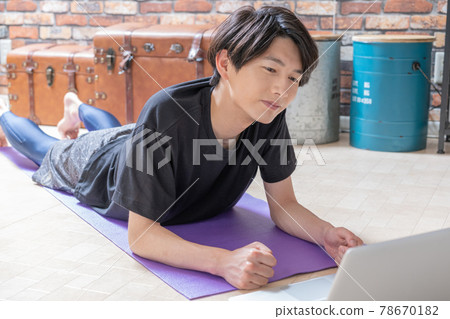 A young man checking muscle training videos on his computer while lying down in his living room early in the morning A young man checking muscle training videos on his computer while lying down in his living room early in the morning 78670182