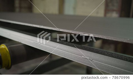 Continuous sheet of metallic material being fed through machine. Metal sheet on the conveyor. Painting large metal sheets in a factory Continuous sheet of metallic material being fed through machine. Metal sheet on the conveyor. Painting large metal sheets in a factory 78670996