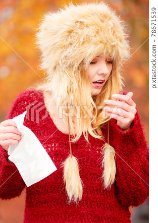 Sick woman in autumn park sneezing into tissue. Sick woman in autumn park sneezing into tissue. 78671539