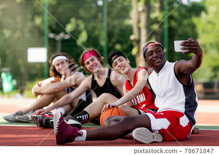Team of happy basketball players taking selfie while relaxing after game at outdoor stadium, blank space 78671847