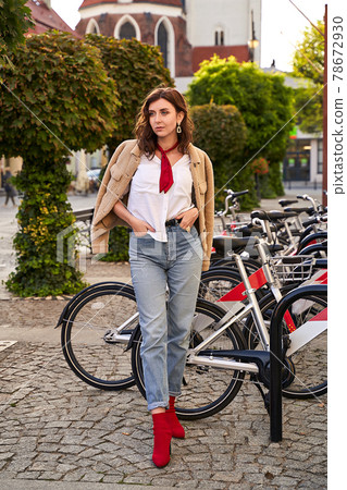 Young beautiful woman in red high heel shoes, blue denim jeans pants and teddy jacket coat posing on street bicycle rental parking background in European city Young beautiful woman in red high heel shoes, blue denim jeans pants and teddy jacket coat posing on street bicycle rental parking background in European city 78672930