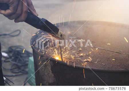 The technical Industry worker welding iron pieces tank at work with a spark flash light 78673576