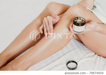 woman applying body butter on legs after shugaring procedure. depilation and after shave skin care concept 78674850