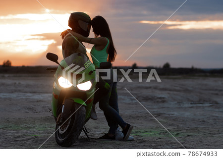 Couple embracing near motorbike on beach at sunset 78674933