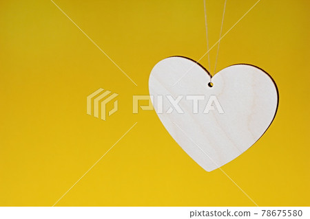 A wooden heart is hanging on a string on a yellow background. A wooden heart is hanging on a string on a yellow background. 78675580