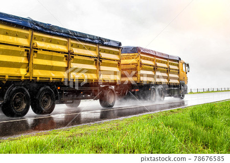 Yellow modern grain truck transporting grain in rainy weather on the highway, in the background. Slippery road, agribusiness, wet weather 78676585