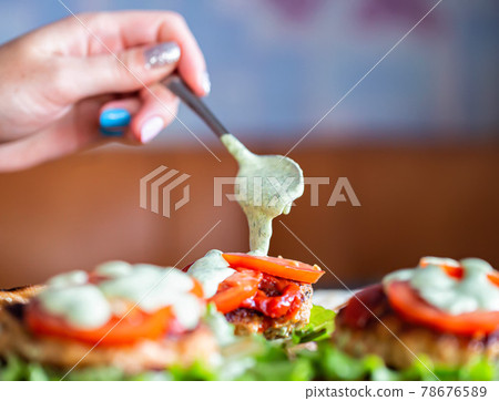 The girl puts sauce on homemade burgers with a spoon. Cooking delicious fast food at home, close-up The girl puts sauce on homemade burgers with a spoon. Cooking delicious fast food at home, close-up 78676589