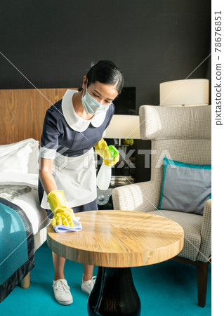 Young female in protective mask and uniform cleaning table 78676851