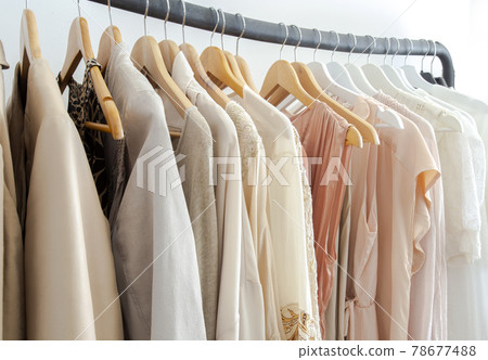 Stylish womans clothes hanging on a rack natural colors, trending concept,pastel colors in white room modern design closeup Stylish womans clothes hanging on a rack natural colors, trending concept,pastel colors in white room modern design closeup 78677488