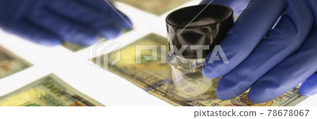 Man in gloves checking counterfeit money with magnifying glass closeup 78678067