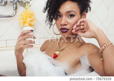 young afro-american teen girl laying in bath with foam, wearing swag jewelry flawless, making selfie 78679209