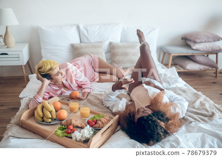 Two women in sleeping clothes lying on bed communicating Two women in sleeping clothes lying on bed communicating 78679379