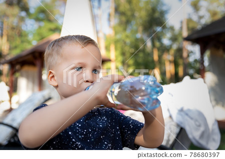 Portrait of cute playful little caucasian blond thirsty toddler boy kid holding plastic bottle and drinking water on hot summer day outdoors. Children heat dehydration danger awareness 78680397