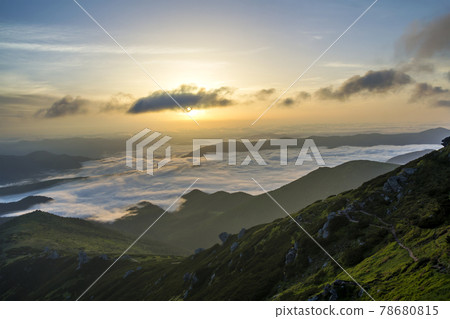 Fantastic view of mountain valley covered with low white puffy like snow clouds stretching to foggy horizon under bright morning sky with light orange glow at sunrise. Beauty of nature concept. 78680815