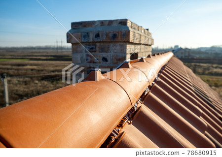 Closeup of yellow ceramic roofing ridge tiles on top of residential building roof under construction. Closeup of yellow ceramic roofing ridge tiles on top of residential building roof under construction. 78680915