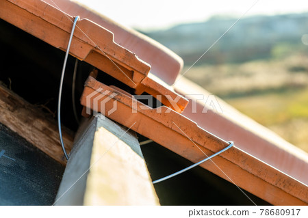 Closeup of metal montage anchor for installation of yellow ceramic roofing tiles mounted on wooden boards covering residential building roof under construction. Closeup of metal montage anchor for installation of yellow ceramic roofing tiles mounted on wooden boards covering residential building roof under construction. 78680917