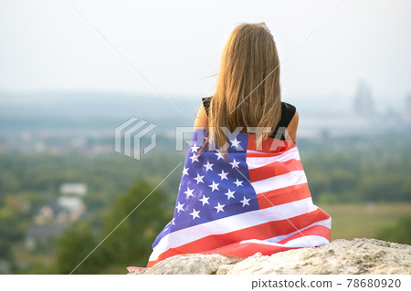 Young happy woman with long hair holding waving on wind american national flag on her sholders resting outdoors enjoying warm summer day. Young happy woman with long hair holding waving on wind american national flag on her sholders resting outdoors enjoying warm summer day. 78680920